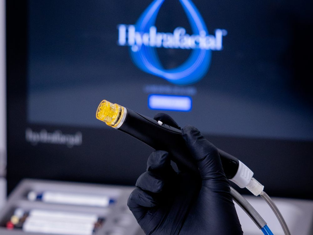 Mano con guante sosteniendo el aplicador de Hydrafacial ante la pantalla del equipo